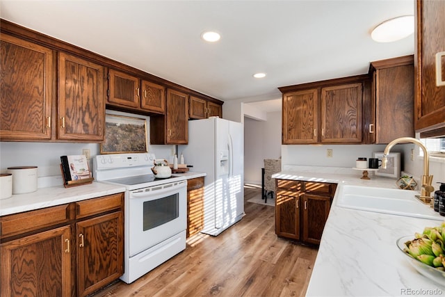 kitchen featuring light wood finished floors, recessed lighting, white appliances, and a sink