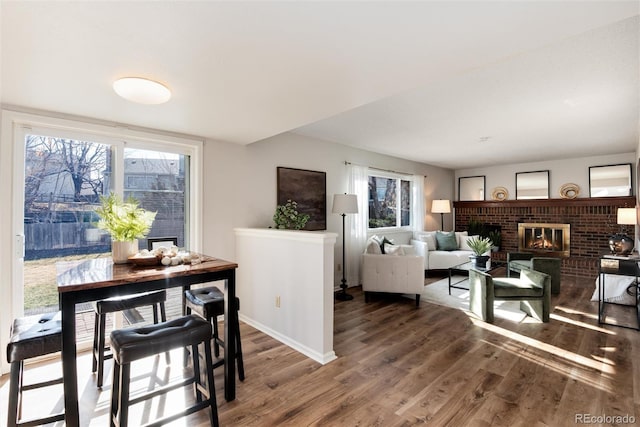 dining space with a healthy amount of sunlight, a brick fireplace, baseboards, and wood finished floors