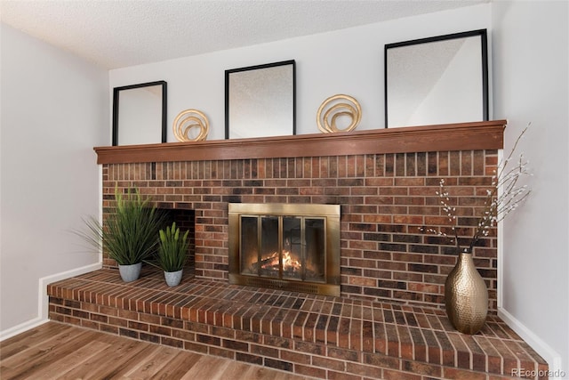 room details with a brick fireplace, a textured ceiling, baseboards, and wood finished floors