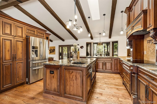 kitchen with pendant lighting, light wood-type flooring, stainless steel fridge with ice dispenser, dark stone countertops, and lofted ceiling with skylight