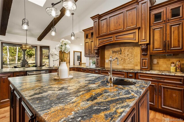 kitchen with a center island with sink, pendant lighting, backsplash, light wood-type flooring, and dark stone countertops