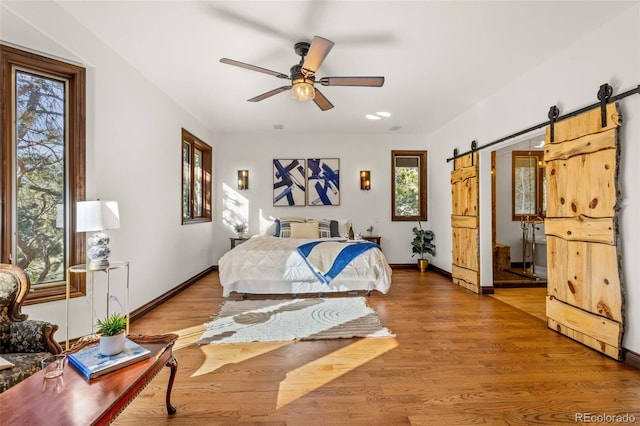 bedroom featuring hardwood / wood-style floors, ceiling fan, and a barn door