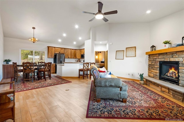 living room with a fireplace, light hardwood / wood-style flooring, ceiling fan, and high vaulted ceiling