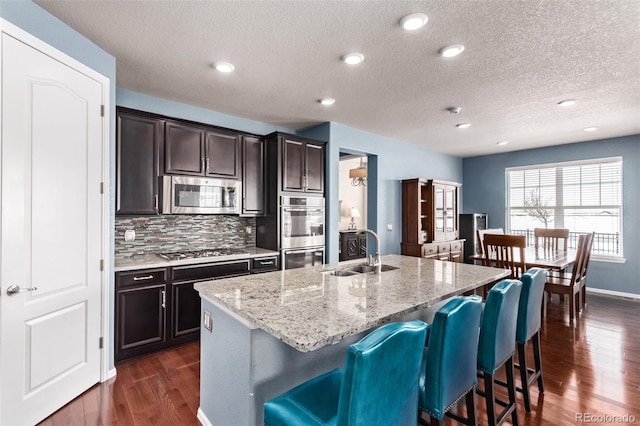 kitchen with sink, a kitchen island with sink, dark hardwood / wood-style floors, a breakfast bar, and appliances with stainless steel finishes