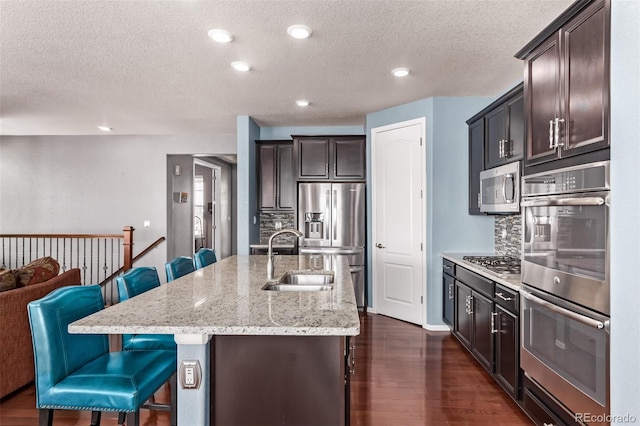 kitchen with dark wood-type flooring, a center island with sink, sink, a kitchen breakfast bar, and appliances with stainless steel finishes