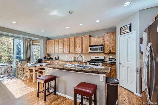 kitchen with a breakfast bar area, appliances with stainless steel finishes, an island with sink, light hardwood / wood-style floors, and sink