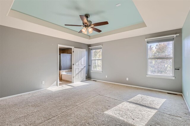 unfurnished bedroom featuring ensuite bathroom, light colored carpet, a tray ceiling, and ceiling fan