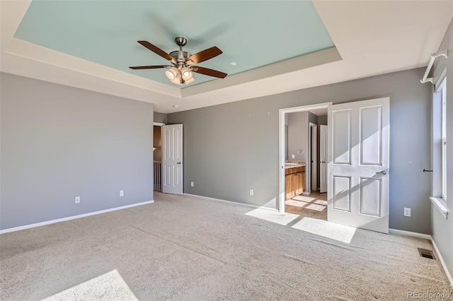 unfurnished bedroom featuring light carpet, ensuite bathroom, ceiling fan, and a raised ceiling