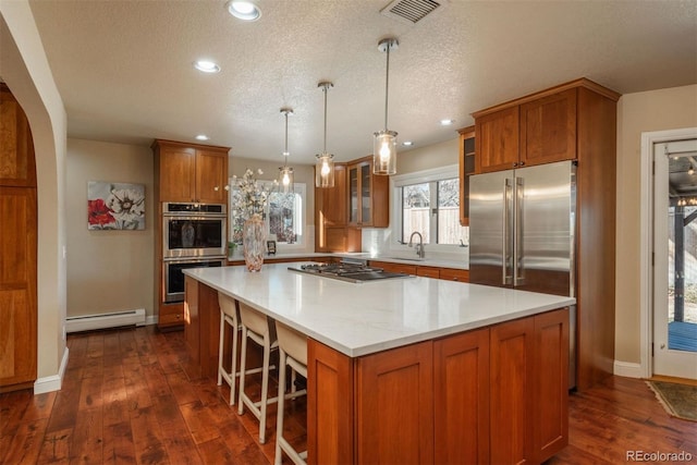 kitchen with a baseboard radiator, hanging light fixtures, a center island, stainless steel appliances, and light stone countertops