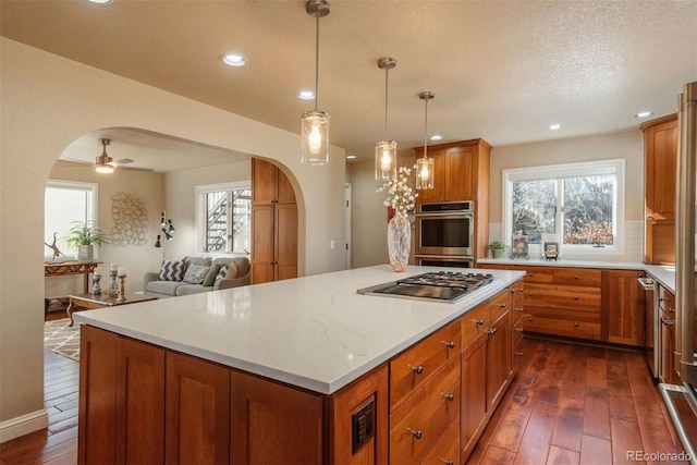 kitchen with stainless steel appliances, dark hardwood / wood-style floors, light stone countertops, a kitchen island, and decorative light fixtures