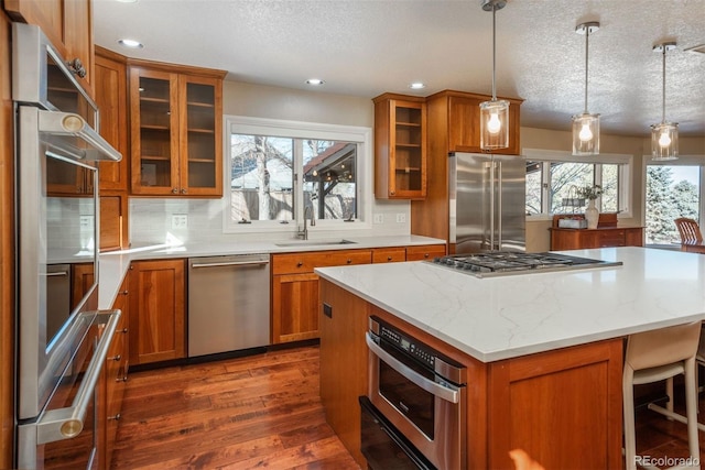 kitchen with appliances with stainless steel finishes, decorative light fixtures, sink, and a kitchen island