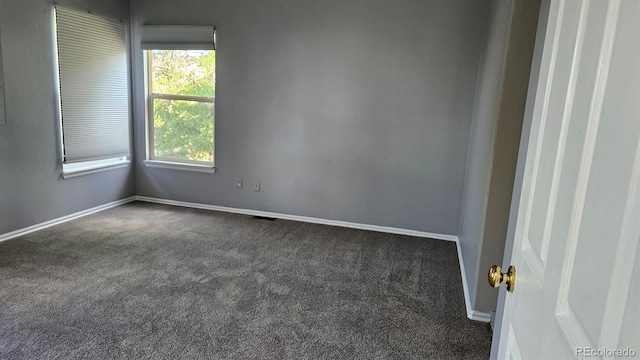 spare room featuring baseboards and dark carpet
