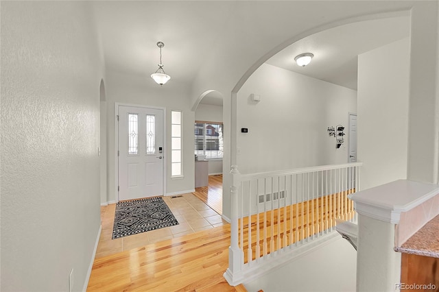 entrance foyer with arched walkways, baseboards, and light wood finished floors