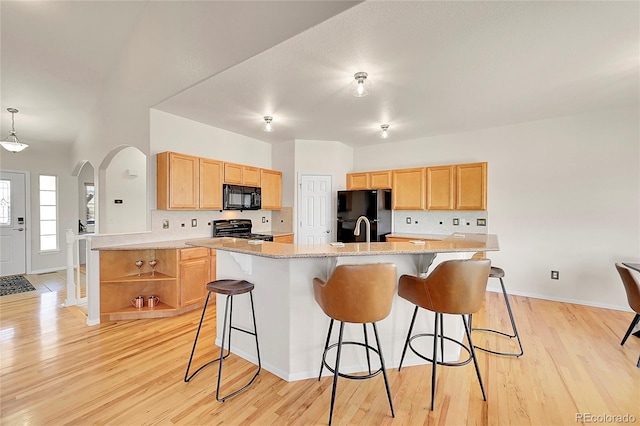 kitchen with light wood-style floors, arched walkways, light brown cabinets, and black appliances