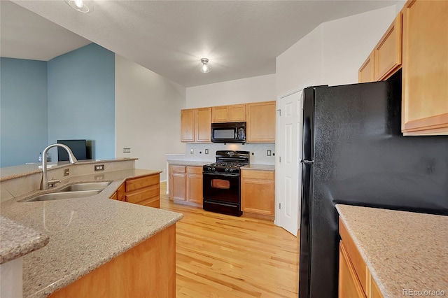 kitchen with a sink, light wood-style flooring, black appliances, and light brown cabinetry