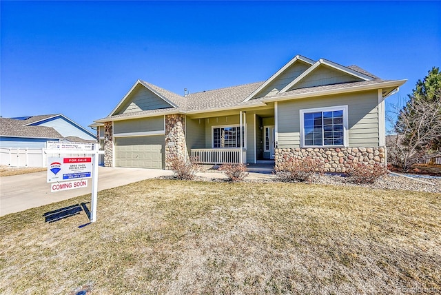 ranch-style home with a garage, covered porch, stone siding, concrete driveway, and roof with shingles