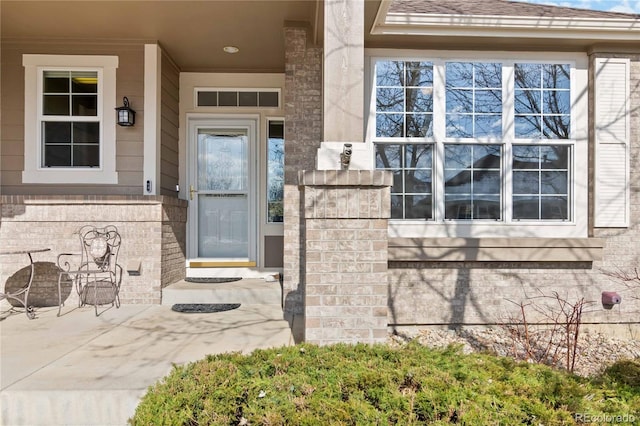 property entrance featuring brick siding, visible vents, and roof with shingles