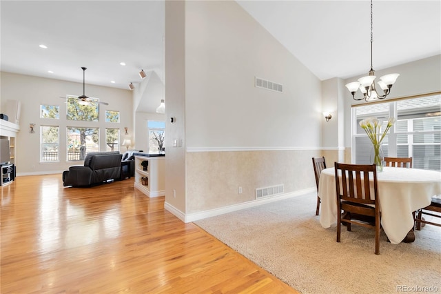 dining space featuring high vaulted ceiling, light wood-style flooring, visible vents, and ceiling fan with notable chandelier