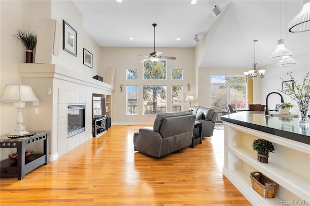 living room featuring baseboards, a tile fireplace, ceiling fan with notable chandelier, light wood-type flooring, and recessed lighting