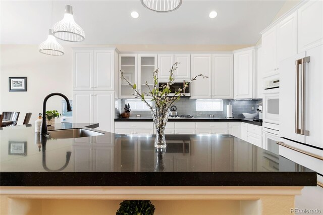 kitchen with glass insert cabinets, stainless steel microwave, pendant lighting, and white cabinets