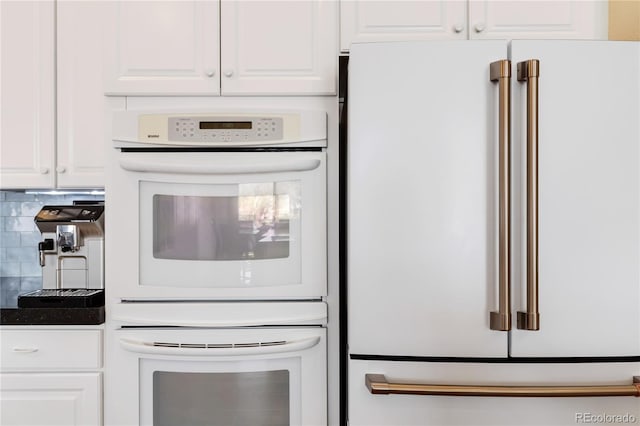 kitchen with tasteful backsplash, white appliances, dark countertops, and white cabinets