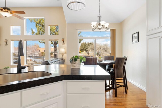 kitchen with light wood finished floors, dark countertops, hanging light fixtures, white cabinetry, and a sink