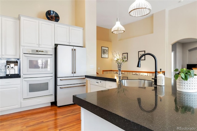 kitchen with pendant lighting, dark countertops, white cabinets, a sink, and white appliances