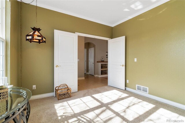 bedroom with light carpet, visible vents, arched walkways, baseboards, and ornamental molding