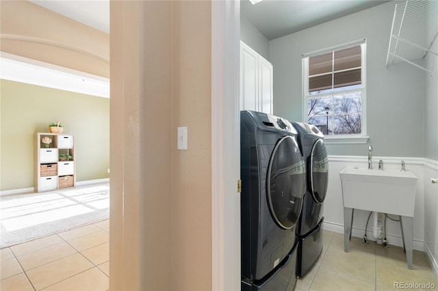 clothes washing area featuring cabinet space, baseboards, washer and clothes dryer, and light tile patterned flooring