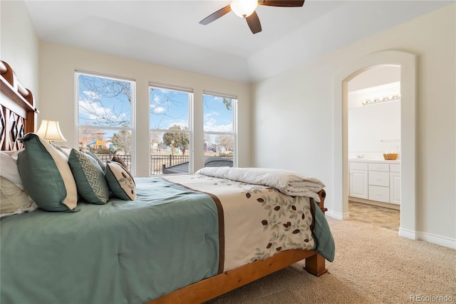 bedroom with baseboards, arched walkways, a ceiling fan, light colored carpet, and ensuite bathroom