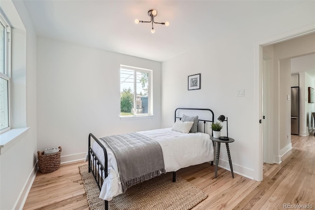 bedroom with light wood-style floors, baseboards, and freestanding refrigerator