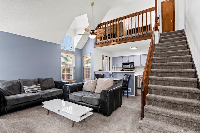living room featuring stairway, high vaulted ceiling, ceiling fan, and light colored carpet