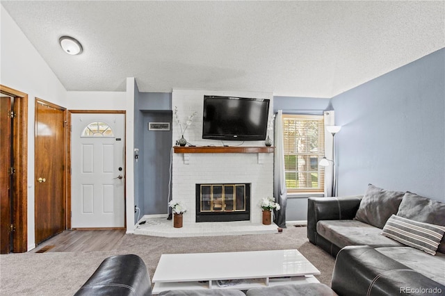 living room with a brick fireplace, a textured ceiling, wood finished floors, and lofted ceiling