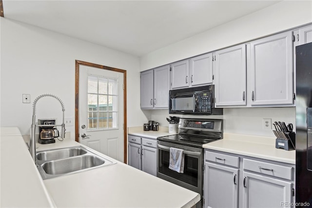 kitchen with stainless steel range with electric stovetop, black microwave, light countertops, gray cabinets, and a sink