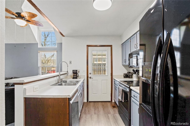 kitchen featuring a sink, light countertops, black appliances, a peninsula, and light wood-style flooring