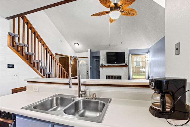 kitchen featuring ceiling fan, a sink, a brick fireplace, light countertops, and vaulted ceiling