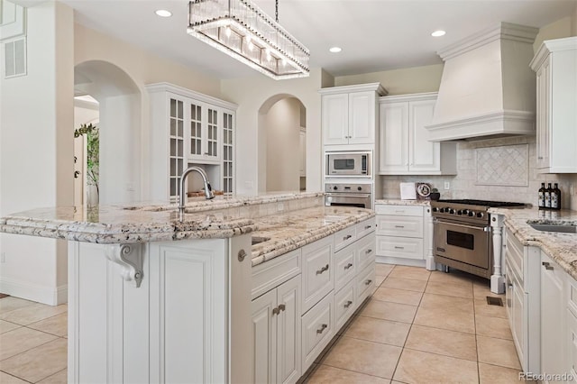 9171 E Harvard Ave, Denver, CO 80231 - kitchen with appliances with stainless steel finishes, custom range hood, arched walkways, light tile patterned floors, and white cabinetry
