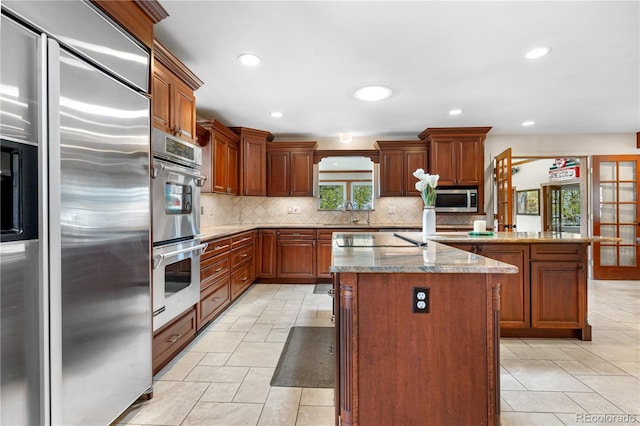 kitchen featuring decorative backsplash, a center island, light stone countertops, stainless steel appliances, and recessed lighting
