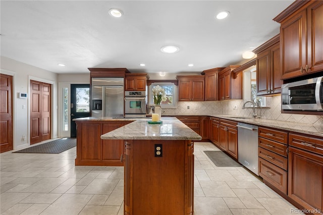 kitchen with light stone countertops, a sink, stainless steel appliances, decorative backsplash, and a kitchen island