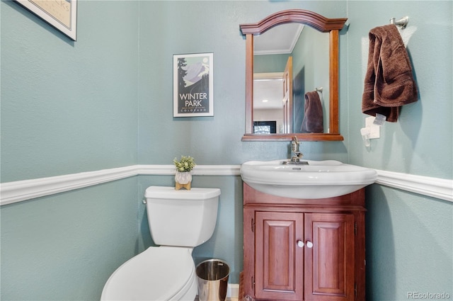 half bath featuring vanity, ornamental molding, and toilet