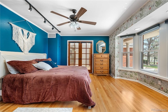 bedroom featuring french doors, rail lighting, wood finished floors, baseboards, and wallpapered walls