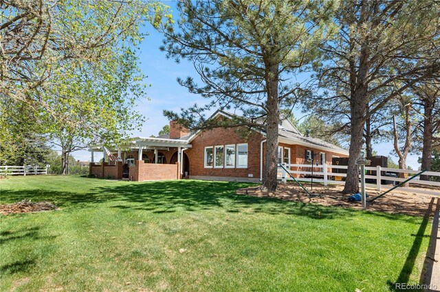 rear view of house with a chimney, a lawn, brick siding, fence, and a pergola