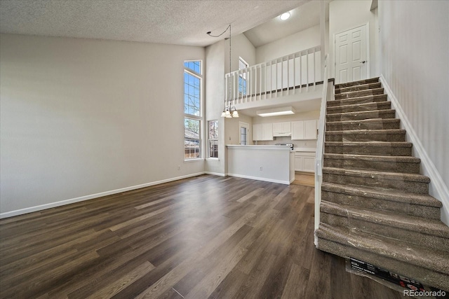 unfurnished living room with dark wood finished floors, stairway, a high ceiling, a textured ceiling, and baseboards