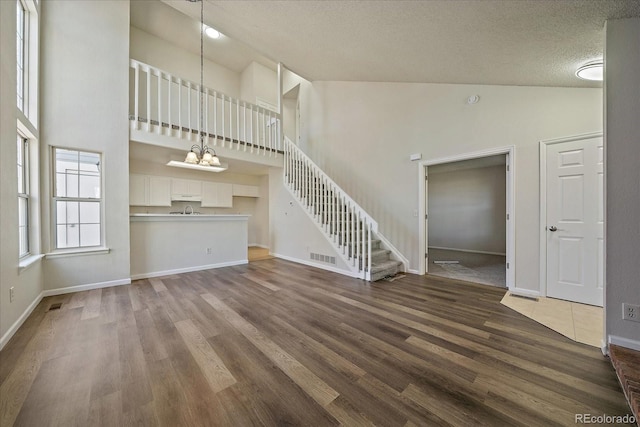 unfurnished living room featuring dark wood-style floors, high vaulted ceiling, baseboards, stairway, and a chandelier