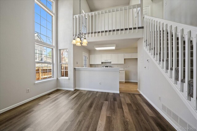 unfurnished living room featuring a towering ceiling, baseboards, plenty of natural light, and dark wood-style floors
