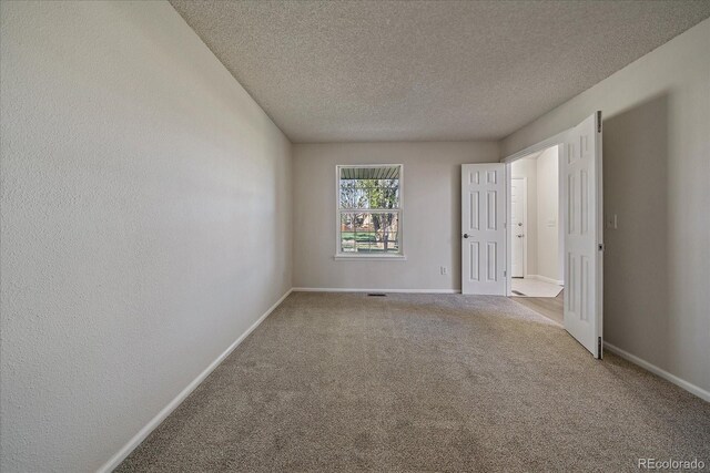 carpeted spare room featuring a textured ceiling, baseboards, and a textured wall