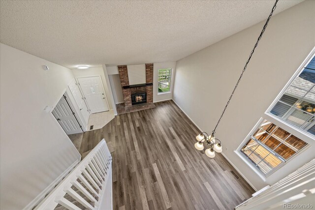 unfurnished living room featuring a brick fireplace, wood finished floors, a textured ceiling, and baseboards