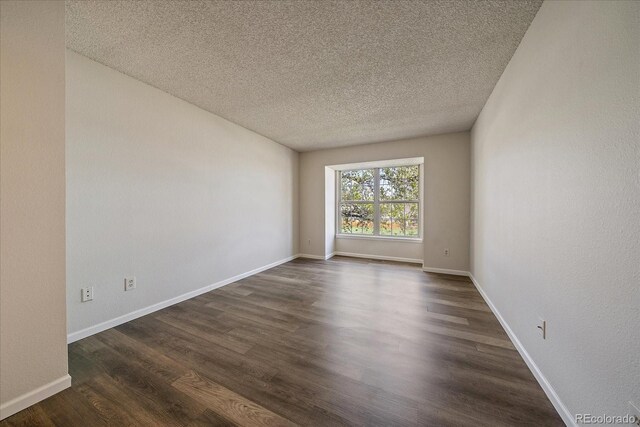 spare room with a textured ceiling, dark wood-style floors, and baseboards
