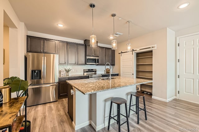 kitchen with dark brown cabinets, light wood finished floors, appliances with stainless steel finishes, and a sink