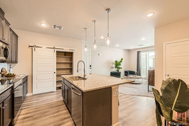kitchen featuring light wood-style flooring, a barn door, visible vents, a sink, and appliances with stainless steel finishes